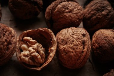 Birkaç cevizin detaylı makro görüntüsü ve bir tanesi çatladı, içerideki çekirdek desenli bir yüzeye yerleştirildi. Toprak tonları, doğal ışık.