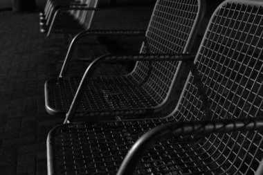 Düşük ışıkta çekilen bir sıra metal kafes bankları karamsar ve minimalist siyah ve beyaz bir kompozisyon oluşturuyor.. 