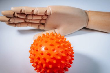 Ahşap bir mankenin eli parlak bir turuncu, keskin bir masaj topunun arkasında yumuşak ışıklandırmalı yumuşak bir yüzey üzerinde.