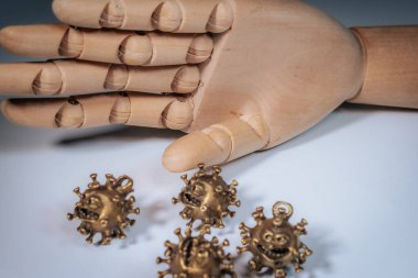 Tahta bir mankenin eli birkaç bronz virüs şekilli heykelciğin üzerinde asılı. Yüzleri aydınlık bir yüzeyde..