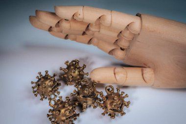 Tahta bir mankenin eli birkaç bronz virüs şekilli heykelciğin üzerinde asılı. Yüzleri aydınlık bir yüzeyde..