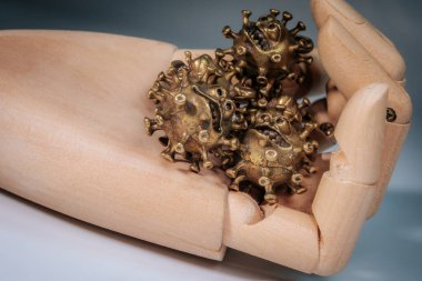 Tarafsız bir arkaplana yerleştirilmiş, stilize edilmiş virüsler şeklinde birkaç bronz heykeli tutan bir elin yakın çekimi.