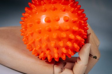 Ahşap bir mankenin eli, parlak turuncu, keskin bir masaj topunu, yumuşak, nötr bir arka plana dikkatlice tutar..