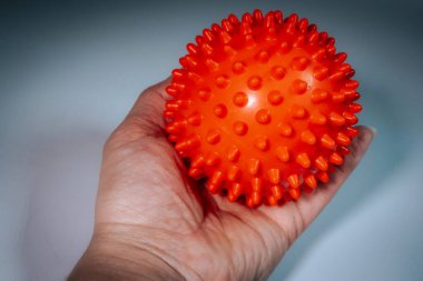 Bir insan eli parlak turuncu dikenli bir masaj topunu fotokopi alanı olan tarafsız bir arka plana karşı tutar. Görünürde logo ya da tanınabilir birey yok.