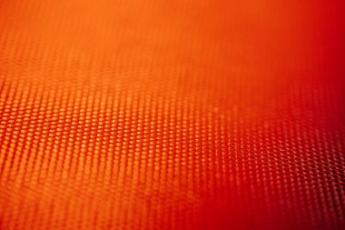 Kafes desenli ve yumuşak ışıklandırmalı turuncu sentetik kumaşın makro görüntüsü. Arkaplan olarak kullanmak için ideal.