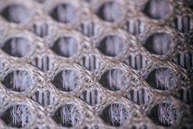 Tekrar eden dairesel dokuma deseni ve görünür iç lifleri olan solunabilir ağ kumaşının yakın plan görüntüsü..