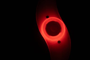 Karanlık bir ortamda parıldayan kırmızı bir LED bisiklet tekerleği ışığının yakın plan görüntüsü, şeffaf, eğimli tasarımı ve güvenlik artırıcı aydınlatması.