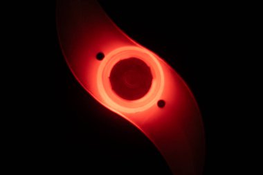 Karanlık bir ortamda parıldayan kırmızı bir LED bisiklet tekerleği ışığının yakın plan görüntüsü, şeffaf, eğimli tasarımı ve güvenlik artırıcı aydınlatması.