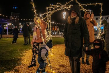 Çocukları ve tatil süslemeleri de dahil olmak üzere kış kıyafetleri giyen insanlar, geceleri bir tatil ışığı tesisini keşfediyorlar.. 