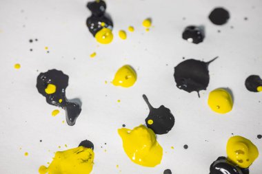 Kalın ve parlak siyah ve sarı boya damlaları beyaz kağıda saçılmış, geniş bir alanda cesur bir soyut düzenleme yaratıyor..