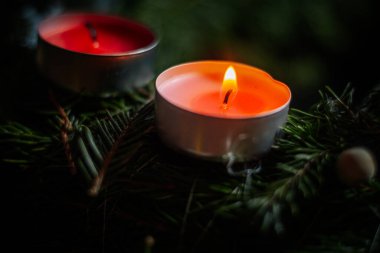 İki kırmızı ve pembe çaydanlık çam dallarında oturur; bir mum sessizce yanar, diğeri yanmaz. Kontrastlı neşeli bir atmosfer..