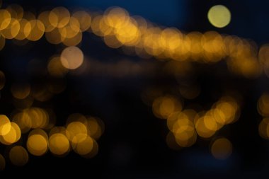 Karanlık bir arka plan karşısında sıcak, altın renkli Bokeh ışıklarının soyut bir görüntüsü, yumuşak, rüya gibi bir ışıltı yaratır..