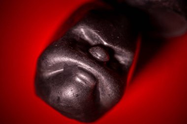 Parlak, siyah voodoo bebeği kafasının parlak kırmızı bir arka plana yerleştirilmiş uç makro görüntüsü. Yüzey parlak ve desenli görünüyor..