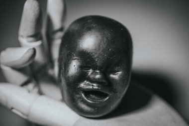 Koyu renkli, yontulmuş bir yüzün tek renkli bir görüntüsü, hafif ahşap bir mankenin koluyla çerçevelenmiş, karşıtlığı, dokuyu ve duyguyu bir metin alanı ile bulanık bir zemine karşı gösteriyor..