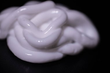 Pürüzsüz siyah bir yüzey üzerinde uzanan sarmalanmış beyaz krem kıvrımlı parlak dokusu ve dramatik ışıklandırmasıyla. Çoklu kopyalama alanı içerir.