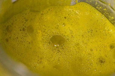 Cam bir kavanozda ince kabarcıkları olan yoğun sarı köpük ince yansımaları olan parlak bir doku yaratıyor ve arka planda çok az yer alıyor..