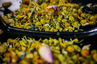 Dağılmış papatya çiçekleri ve renkli yapraklar karanlık bir yüzeydeki eğri bir aynaya yansıyarak desenli, doğal bir bileşim oluşturur..