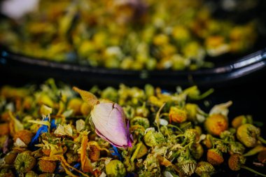 Dağılmış papatya çiçekleri ve renkli yapraklar karanlık bir yüzeydeki eğri bir aynaya yansıyarak desenli, doğal bir bileşim oluşturur..