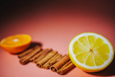 Limon, portakal ve tarçın çubuklarının yakın plan çekimleri. Pembe ve koyu renk arkaplanlarda kesilip, metin için boşluk bırakılıyor. Sahne tazelik ve sıcaklık yayar..