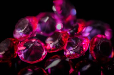 Birkaç kırmızı ve pembe değerli taşın yakın plan parlak yansımaları ve kopyalama alanı olan parlak siyah bir arkaplana saçılmış hali..