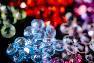 Kırmızı, pembe, mavi ve mor tonlarda parlak değerli taşların yakın planda yansıtıcı aksanları ve arka planda yumuşak bir bokeh etkisi olan parlak siyah bir yüzeye dizilmiş hali..