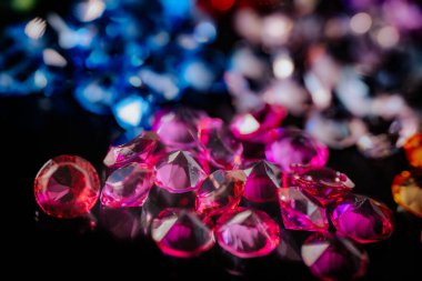 Kırmızı, pembe, mavi ve mor tonlarda parlak değerli taşların yakın planda yansıtıcı aksanları ve arka planda yumuşak bir bokeh etkisi olan parlak siyah bir yüzeye dizilmiş hali..