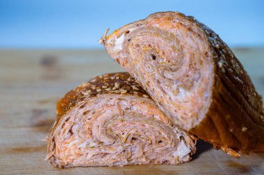 Dilimlenmiş gevrek hamur işi, arka planda bulanık bir ahşap kesim tahtasındaki birden fazla katmanı ve susam tohumunu ortaya çıkarır.