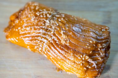 Tahta kesme tahtasına yerleştirilmiş susam tohumlu jöleli somon filetosu canlı rengini ve çekici dokusunu vurguluyor.