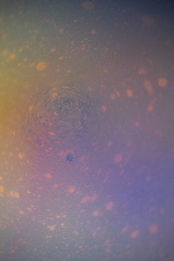 Hassas, kabarcık benzeri noktaları olan, dairesel dalgalanmalar oluşturan pastel sıvının makro soyut bir görüntüsü. Yumuşak mavi, lavanta, şeftali ve sarı renkler rüya gibi bir sıvı doku yaratır..