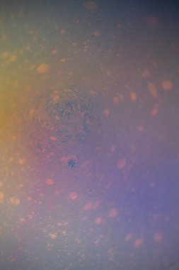 Hassas, kabarcık benzeri noktaları olan, dairesel dalgalanmalar oluşturan pastel sıvının makro soyut bir görüntüsü. Yumuşak mavi, lavanta, şeftali ve sarı renkler rüya gibi bir sıvı doku yaratır..