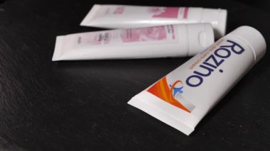 Üç beyaz kozmetik krem tüpten oluşan yakın plan bir fotoğraf. Koyu renkli ahşap bir masaya yapıştırılmış marka etiketleri var. Yumuşak ışıklandırma paketleme ayrıntılarını ve pürüzsüz dokuyu vurgular.