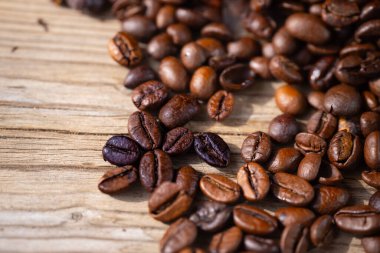 Makro yakın plan kahve çekirdekleri hafif ahşap bir yüzeye saçılmış, zengin dokular, doğal kusurlar ve sığ bir alan derinliğine sahip sıcak tonlarda sergileniyor..