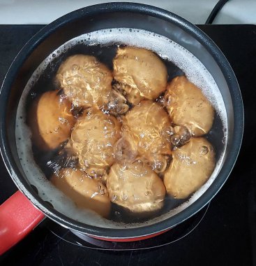 Elektrikli ocağın üzerine yerleştirilmiş bir tencerede birkaç yumurta kaynayan sıcak suda kaynıyor..