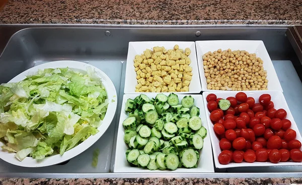 İçinde marul, salatalık, kiraz domatesleri, bebek mısırı ve nohut bulunan renkli bir salata barı..