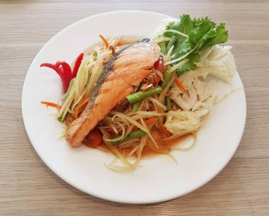 Thai-style papaya salad served with grilled salmon, a fusion of Isaan and international cuisine.
