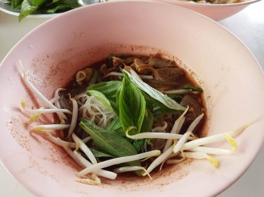 Fesleğen yaprakları ve taze fasulye filizleriyle kaplı zengin ve lezzetli Tayland usulü domuz etli erişte..