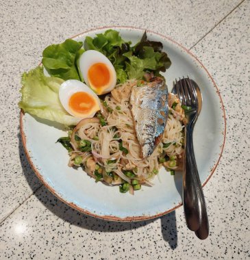 Baharatlı pirinç vermicelli salatası Vietnam sosisi ve fermente balık sosuyla karıştırılmış, üzerine de kalın bir tat vermesi için uskumru konmuş..