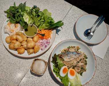 Baharatlı pirinç erişte salatası, uskumru ve taze otlar ve sebzelerle kızartılmış levrek içeren Tayland usulü bir yemek masası..