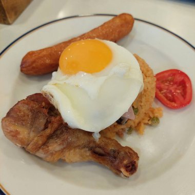 Tayland usulü kızarmış pirinç ketçap ve kuru üzümle pişirilir, sosis, sahanda yumurta, kızarmış tavuk budu ve jambonla servis edilir. Tatlı ve lezzetli lezzetlerin karışımından oluşan popüler konforlu yemek..