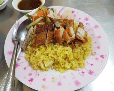 Üstü kızarmış ördek ve gevrek domuz göbeğiyle kaplı sarı pirinç. Bu lezzetli Asya füzyon yemeği turşulu sebzeler ve lezzetli bir sos ile servis edilir..