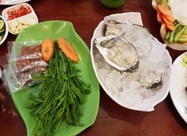 Restoranda ezilmiş buz üzerinde servis edilen büyük taze istiridye manzarası. Geleneksel Tayland baharatlarıyla birlikte akasya yaprakları ve kızarmış arpacık soğanları da dahil..