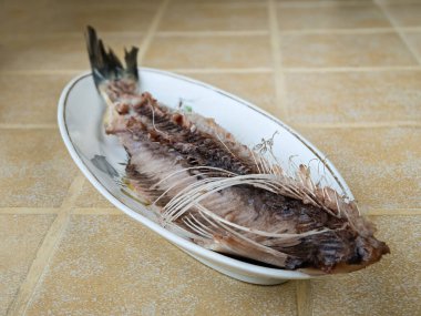 Seramik bir tezgahın üzerinde porselen bir tabakta yarısı kemirilmiş ringa balığı.