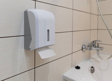 Duvara monte edilmiş tuvalet kağıdı tutacağı kutusunun yakın çekimi modern bir banyo içindeki büyük seramik seramik karolarla tamamlanmış bir duvara dayanır.