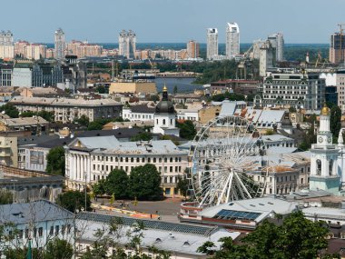 Kyiv, Ukrayna - 22 Haziran 2025: Podil 'in Kyiv' deki panoramik manzarası. Tarihsel Kyiv-Mohyla Akademisi, dönme dolap ve mavi gökyüzünün altındaki kilise kubbeleri. Dinyeper nehri ve Ukrayna 'da şehir silueti olan şehir manzarası.