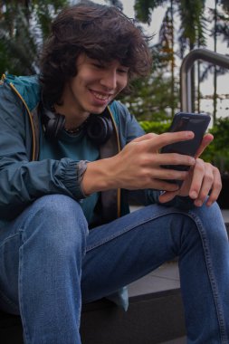 Kapalı kapılar ardında cep telefonuyla merdivenlerde oturan mutlu genç adam.