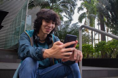 Genç adam şehirde akıllı telefon kullanırken mutlu bir şekilde gülümsüyor.