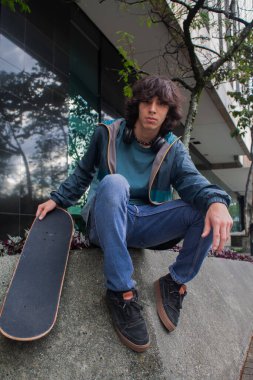 Elinde kaykayla oturan kendinden emin genç bir adam.