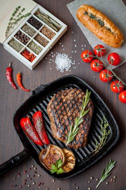 Grilled Steak Ribeye on grill iron pan, chili pepper, salt and rosemary on wooden background clipart