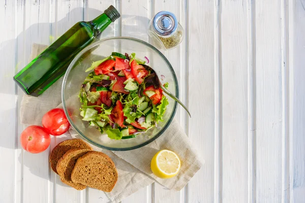 taste of vegetarian summer concept, salad of lettuce leaf, tomato, cucumber, onion, oregano with olive oil and lemon juice on white wooden background with copyspace