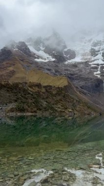 Turkuaz suların Andean 'ın engebeli tepelerini yansıttığı ve yukarıdaki buzuldan eriyen karı yansıttığı yer. Peru 'daki Salkantay patikası boyunca uzanan bu kutsal göl And Dağları' nın ihtişamının ortasında bir huzur ve saygı anı sunuyor..